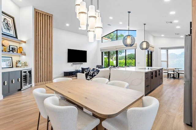 dining space with high vaulted ceiling, light wood-type flooring, a healthy amount of sunlight, and beverage cooler