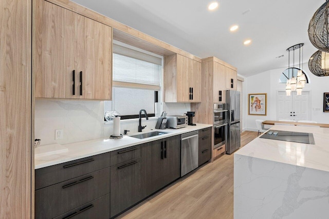 kitchen with light stone counters, appliances with stainless steel finishes, light hardwood / wood-style flooring, sink, and decorative light fixtures