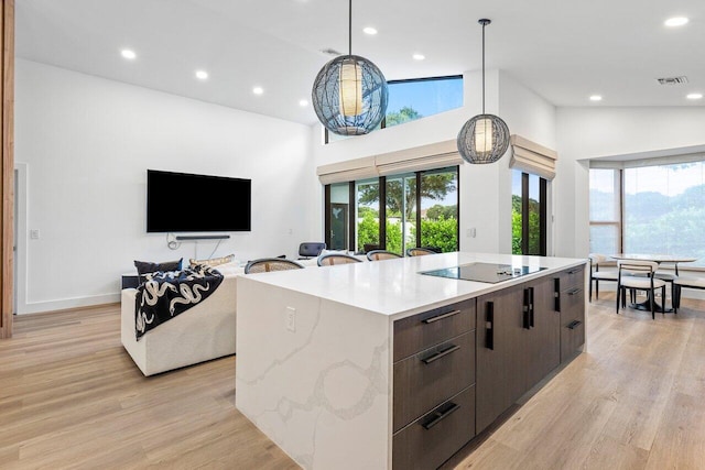 kitchen featuring black electric stovetop, light wood-type flooring, hanging light fixtures, a large island, and high vaulted ceiling