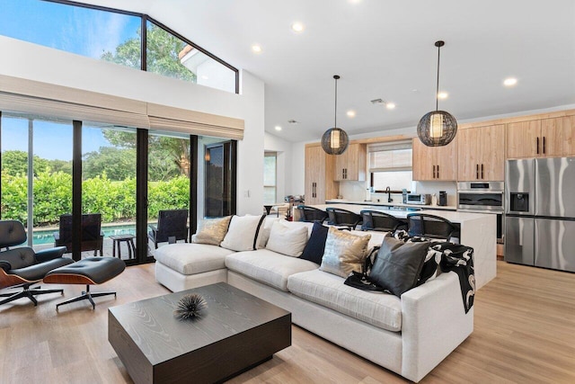 living room with high vaulted ceiling, sink, and light wood-type flooring