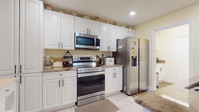 kitchen with white cabinets, light tile patterned flooring, light stone counters, and appliances with stainless steel finishes