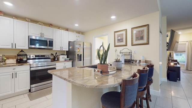 kitchen with a kitchen breakfast bar, light stone counters, stainless steel appliances, light tile patterned floors, and white cabinets