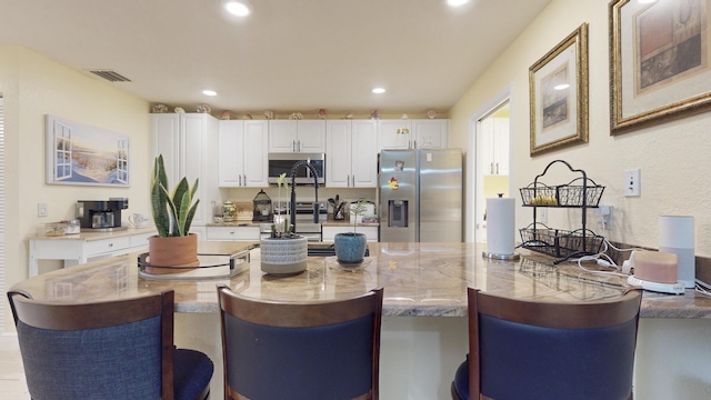 kitchen featuring white cabinets, a kitchen bar, light stone countertops, and stainless steel appliances