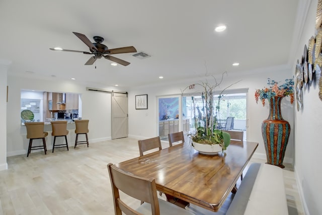 dining room with ceiling fan, a barn door, and light hardwood / wood-style floors