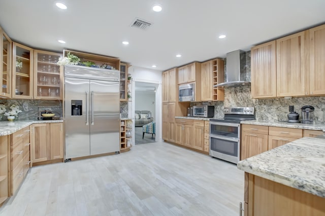 kitchen with decorative backsplash, built in appliances, light hardwood / wood-style floors, and wall chimney exhaust hood