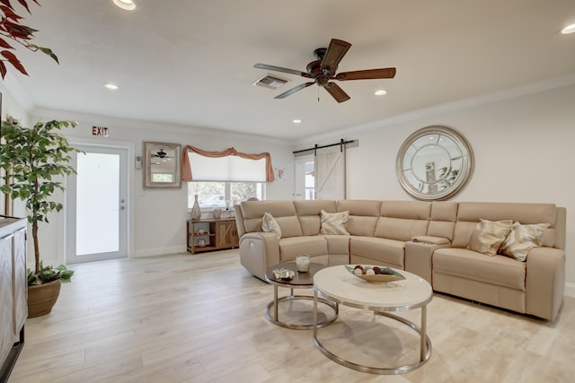 living room with light wood-type flooring, a barn door, ceiling fan, and crown molding