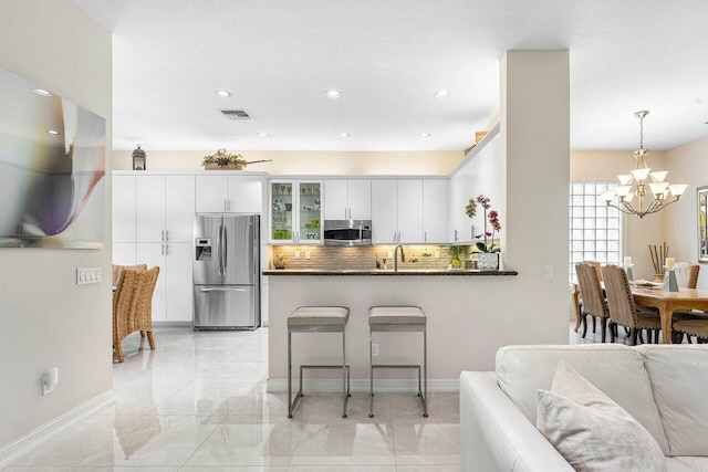 kitchen with stainless steel appliances, white cabinetry, backsplash, decorative light fixtures, and kitchen peninsula