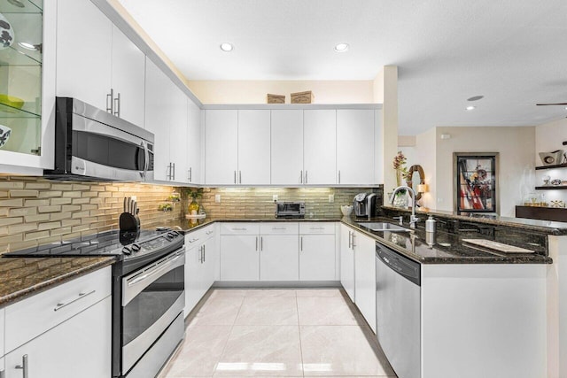 kitchen featuring sink, kitchen peninsula, appliances with stainless steel finishes, dark stone counters, and white cabinets