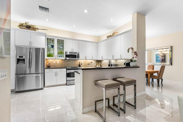 kitchen featuring stainless steel appliances, kitchen peninsula, a textured ceiling, backsplash, and white cabinetry