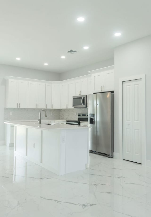 kitchen featuring white cabinetry, sink, appliances with stainless steel finishes, tasteful backsplash, and an island with sink