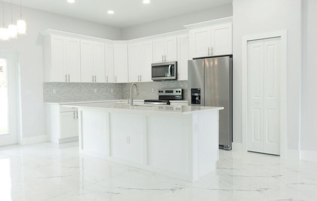 kitchen with stainless steel appliances, backsplash, white cabinetry, decorative light fixtures, and an island with sink