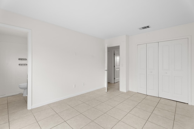 unfurnished bedroom with a closet, ensuite bath, and light tile patterned floors