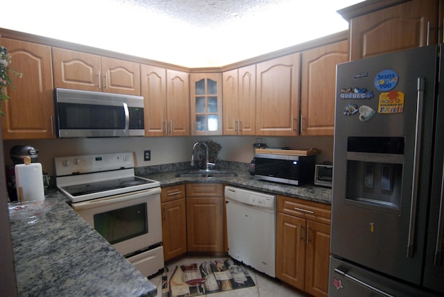 kitchen with a textured ceiling, dark stone countertops, stainless steel appliances, and sink