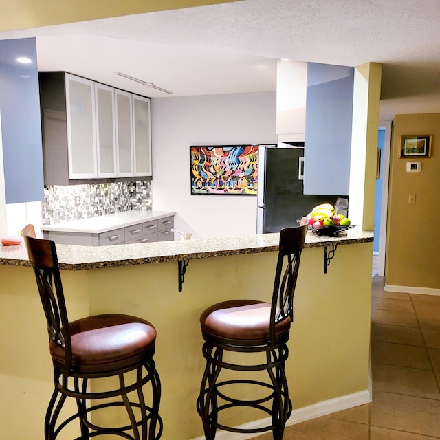 kitchen featuring stainless steel fridge, decorative backsplash, a kitchen bar, and kitchen peninsula