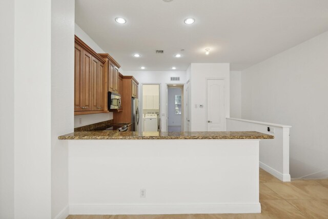 kitchen with kitchen peninsula, ceiling fan, stainless steel appliances, dark stone counters, and sink