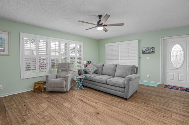 living room with ceiling fan, a textured ceiling, and light wood-type flooring