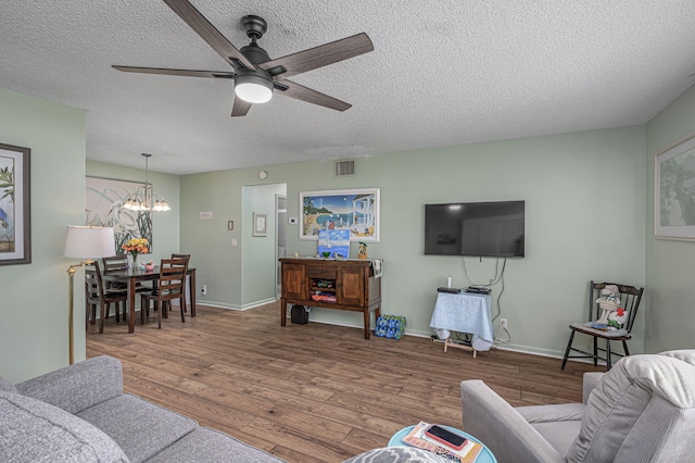 living room with hardwood / wood-style floors, ceiling fan with notable chandelier, and a textured ceiling