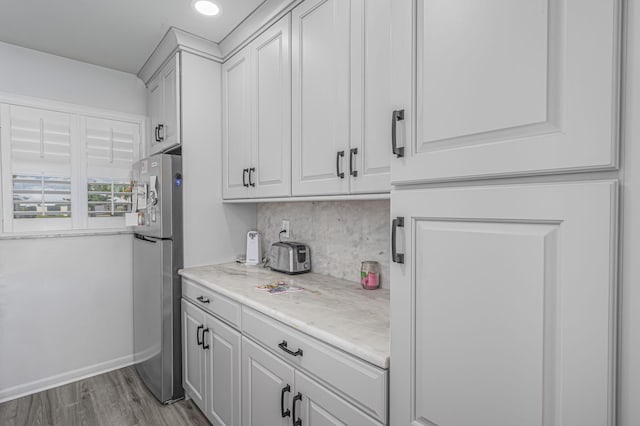 kitchen with light hardwood / wood-style flooring, decorative backsplash, light stone counters, white cabinetry, and stainless steel refrigerator