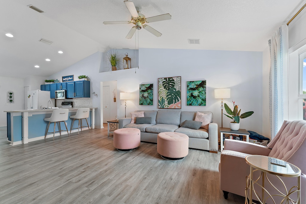 living room with ceiling fan, sink, light wood-type flooring, and lofted ceiling