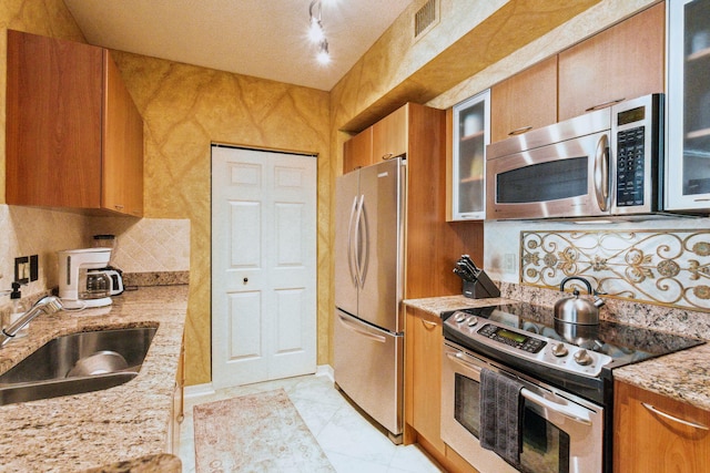 kitchen featuring light stone countertops, light tile patterned flooring, appliances with stainless steel finishes, sink, and backsplash