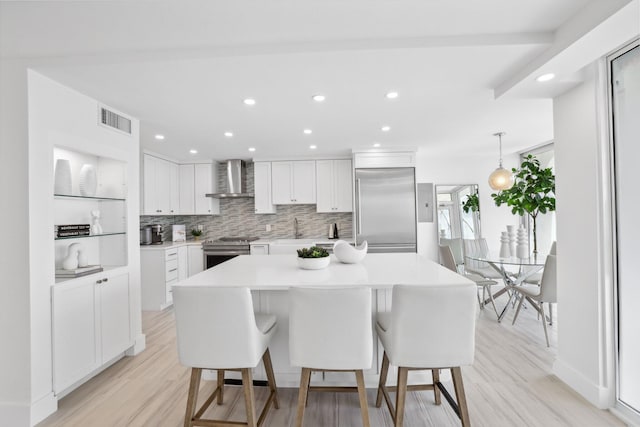 kitchen featuring light hardwood / wood-style floors, wall chimney range hood, white cabinetry, and appliances with stainless steel finishes