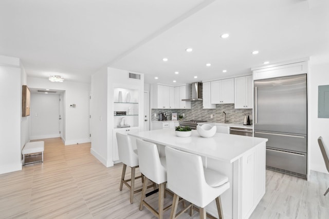 kitchen with a kitchen island, appliances with stainless steel finishes, a kitchen breakfast bar, white cabinets, and wall chimney exhaust hood