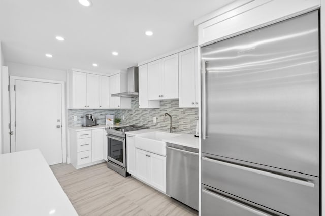 kitchen featuring tasteful backsplash, stainless steel appliances, white cabinetry, sink, and wall chimney exhaust hood