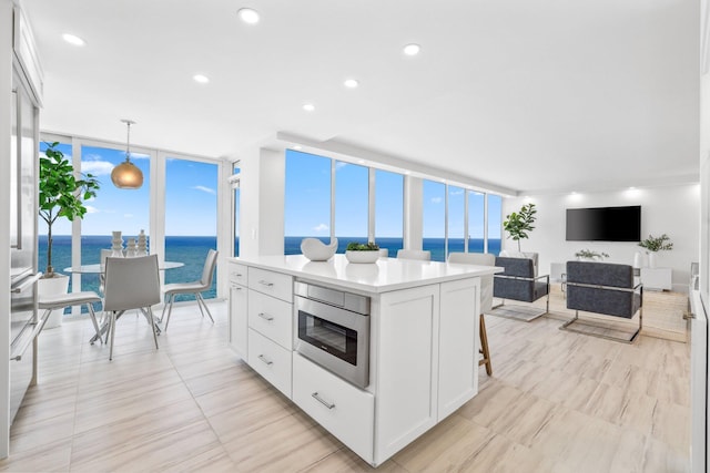 kitchen with a water view, a center island, white cabinets, a wall of windows, and decorative light fixtures