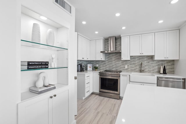 kitchen featuring stainless steel appliances, wall chimney exhaust hood, white cabinetry, and sink