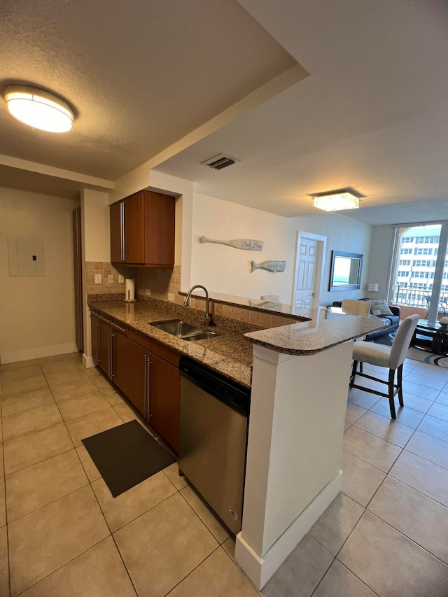 kitchen featuring kitchen peninsula, dark stone countertops, sink, light tile patterned flooring, and stainless steel dishwasher