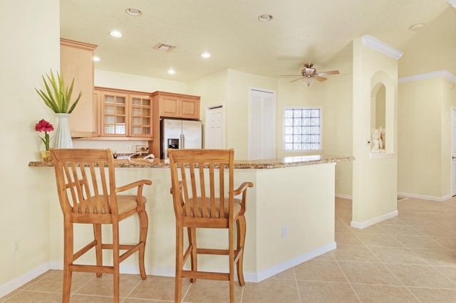 kitchen featuring a peninsula, light stone counters, glass insert cabinets, and stainless steel fridge