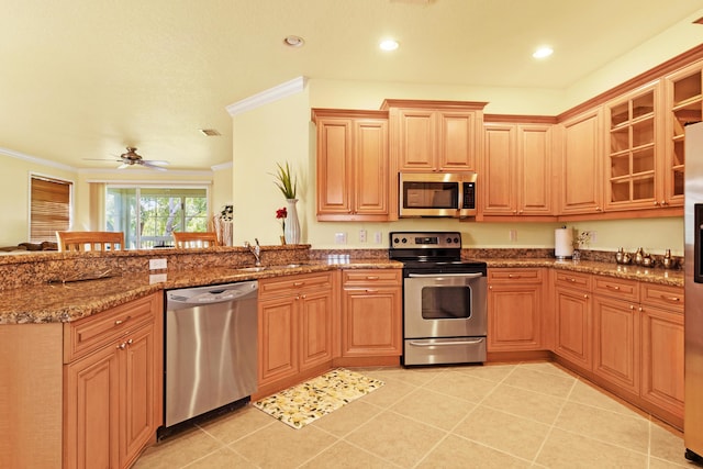 kitchen featuring appliances with stainless steel finishes, dark stone countertops, sink, light tile patterned floors, and crown molding