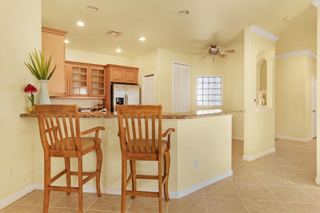 kitchen featuring stainless steel refrigerator with ice dispenser, a breakfast bar area, and light stone counters