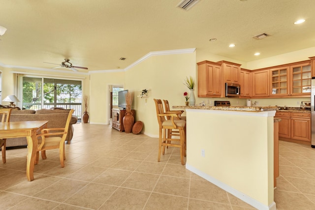 kitchen with light stone countertops, ornamental molding, light tile patterned flooring, ceiling fan, and a breakfast bar