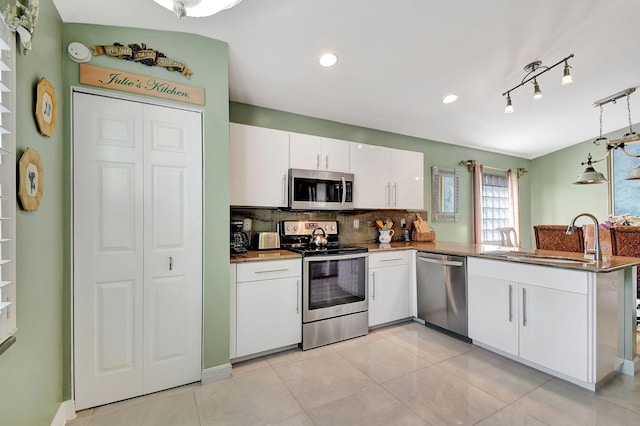 kitchen featuring kitchen peninsula, appliances with stainless steel finishes, sink, white cabinetry, and hanging light fixtures