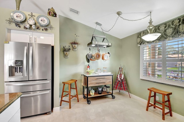 kitchen with lofted ceiling, white cabinets, hanging light fixtures, stone countertops, and stainless steel fridge with ice dispenser