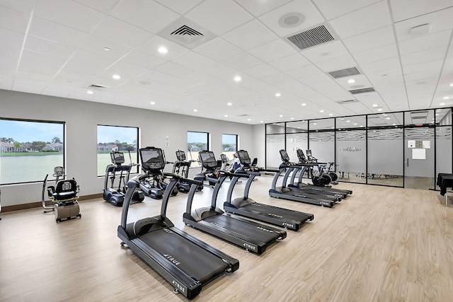 gym with a paneled ceiling, a water view, and light wood-type flooring