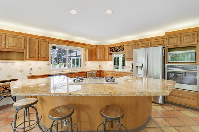 kitchen featuring a breakfast bar area, stainless steel appliances, a kitchen island, backsplash, and brown cabinetry