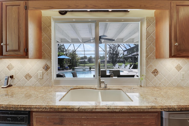 kitchen featuring light stone counters, tasteful backsplash, stainless steel dishwasher, and sink