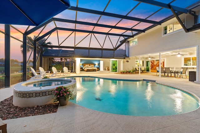 pool at dusk with glass enclosure, a pool with connected hot tub, a patio area, and ceiling fan