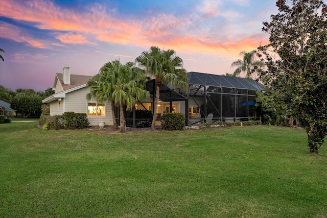 back of house at dusk featuring a lawn, a chimney, and a lanai