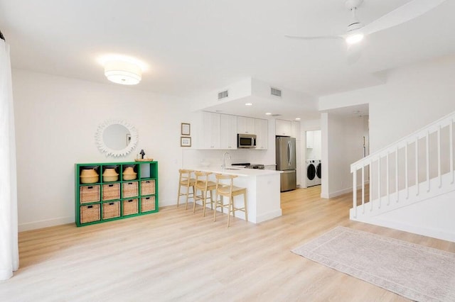 kitchen featuring light hardwood / wood-style flooring, kitchen peninsula, stainless steel appliances, white cabinetry, and washer and dryer