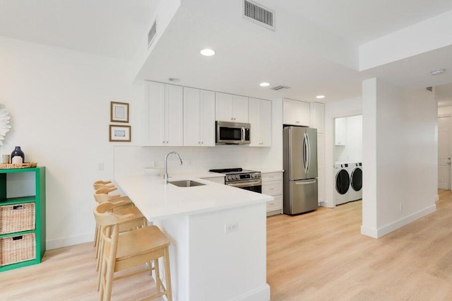 kitchen with appliances with stainless steel finishes, independent washer and dryer, sink, and light hardwood / wood-style floors