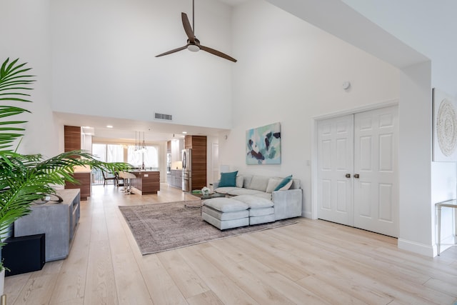 living room with ceiling fan, a towering ceiling, and light hardwood / wood-style floors