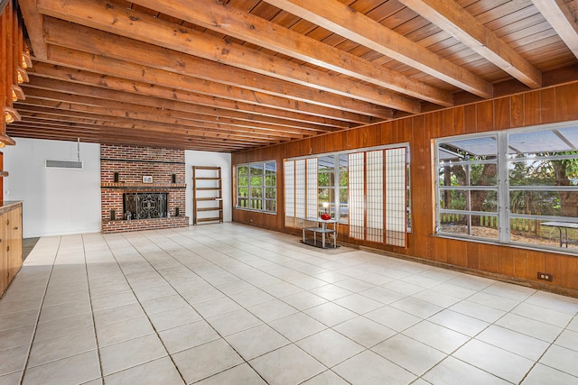 unfurnished living room with light tile patterned flooring, beam ceiling, wood walls, a brick fireplace, and wooden ceiling