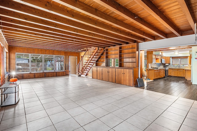 unfurnished living room with wooden ceiling, light tile patterned flooring, sink, beam ceiling, and wooden walls