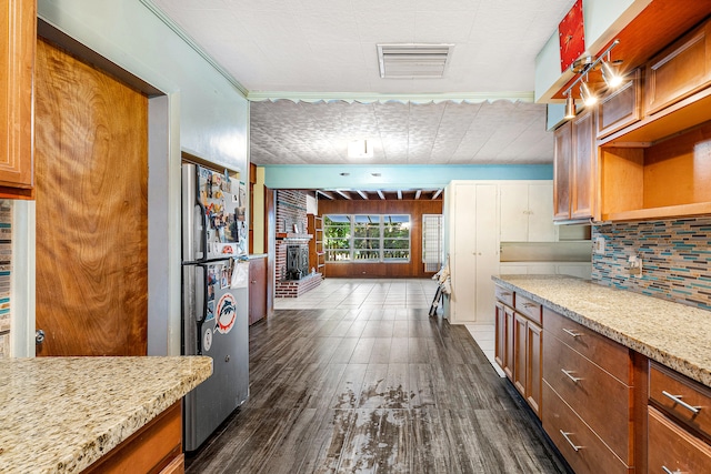 kitchen with crown molding, dark hardwood / wood-style floors, light stone counters, and stainless steel refrigerator