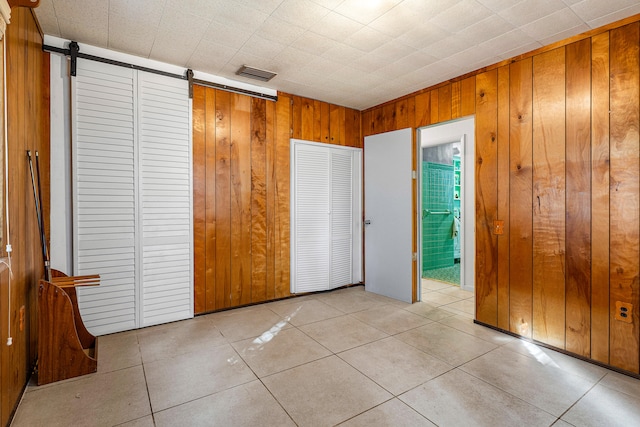 unfurnished bedroom with a barn door, wooden walls, and light tile patterned floors