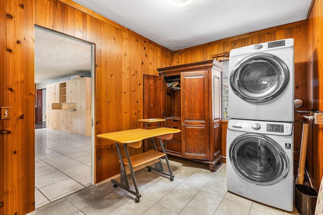 laundry room with cabinets, wood walls, light tile patterned floors, and stacked washer / drying machine