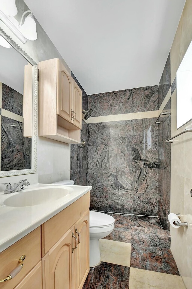 bathroom featuring vanity, toilet, tile walls, and a tile shower